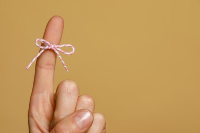 Photo of Woman showing index finger with tied bow as reminder on light brown background, closeup. Space for text