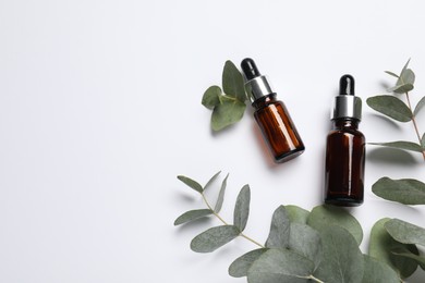 Aromatherapy. Bottles of essential oil and eucalyptus branches on white background, flat lay. Space for text