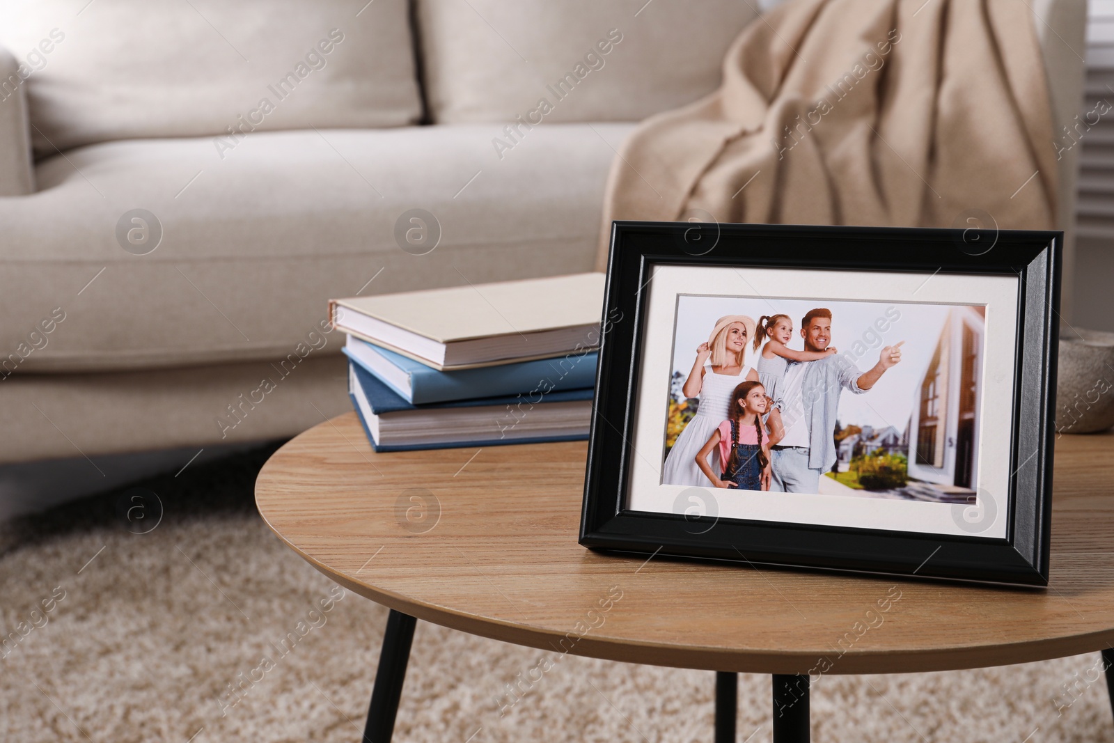 Photo of Frame with family photo and stack of books on wooden coffee table in room, space for text