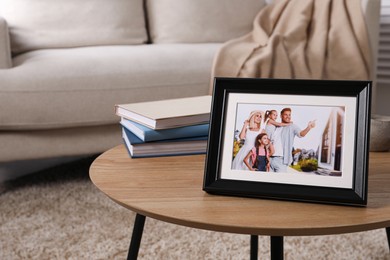 Photo of Frame with family photo and stack of books on wooden coffee table in room, space for text