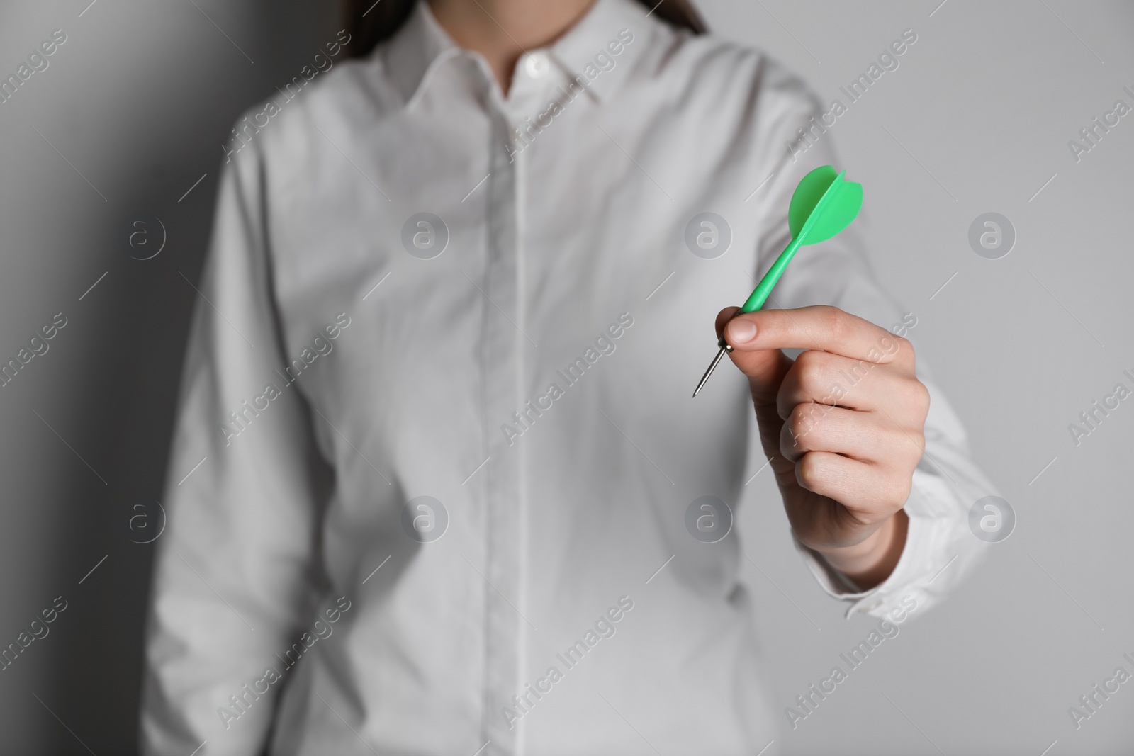 Photo of Businesswoman holding green dart on light background, closeup