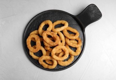 Photo of Slate plate with fried onion rings on grey table, top view