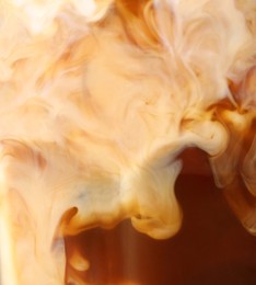 Glass of coffee with milk and ice cubes on blurred background, closeup