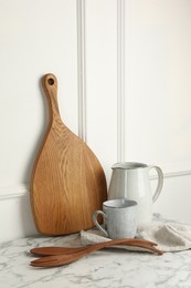 Photo of Wooden cutting board, cutlery and dishware on white marble table
