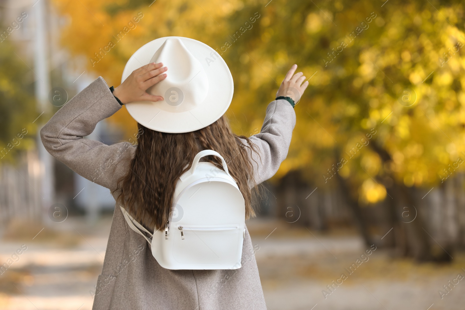 Photo of Young woman with stylish white backpack on city street, back view