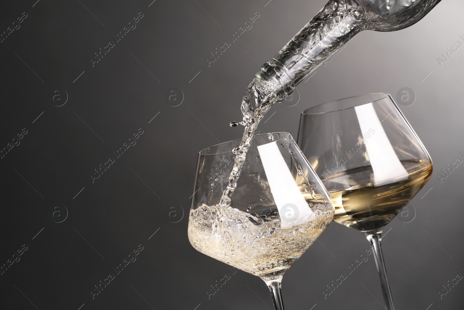 Photo of Pouring white wine into glass against grey background, closeup. Space for text