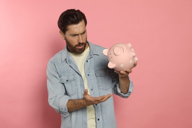 Man with ceramic piggy bank on pale pink background