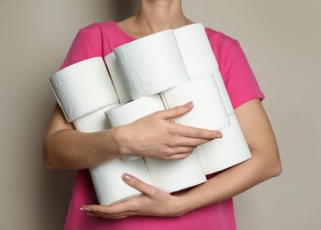 Woman with heap of toilet paper rolls on beige background, closeup