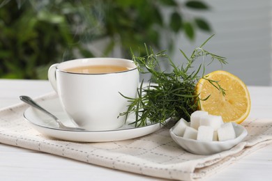 Photo of Aromatic herbal tea, fresh tarragon sprigs, sugar cubes and lemon on white wooden table, closeup