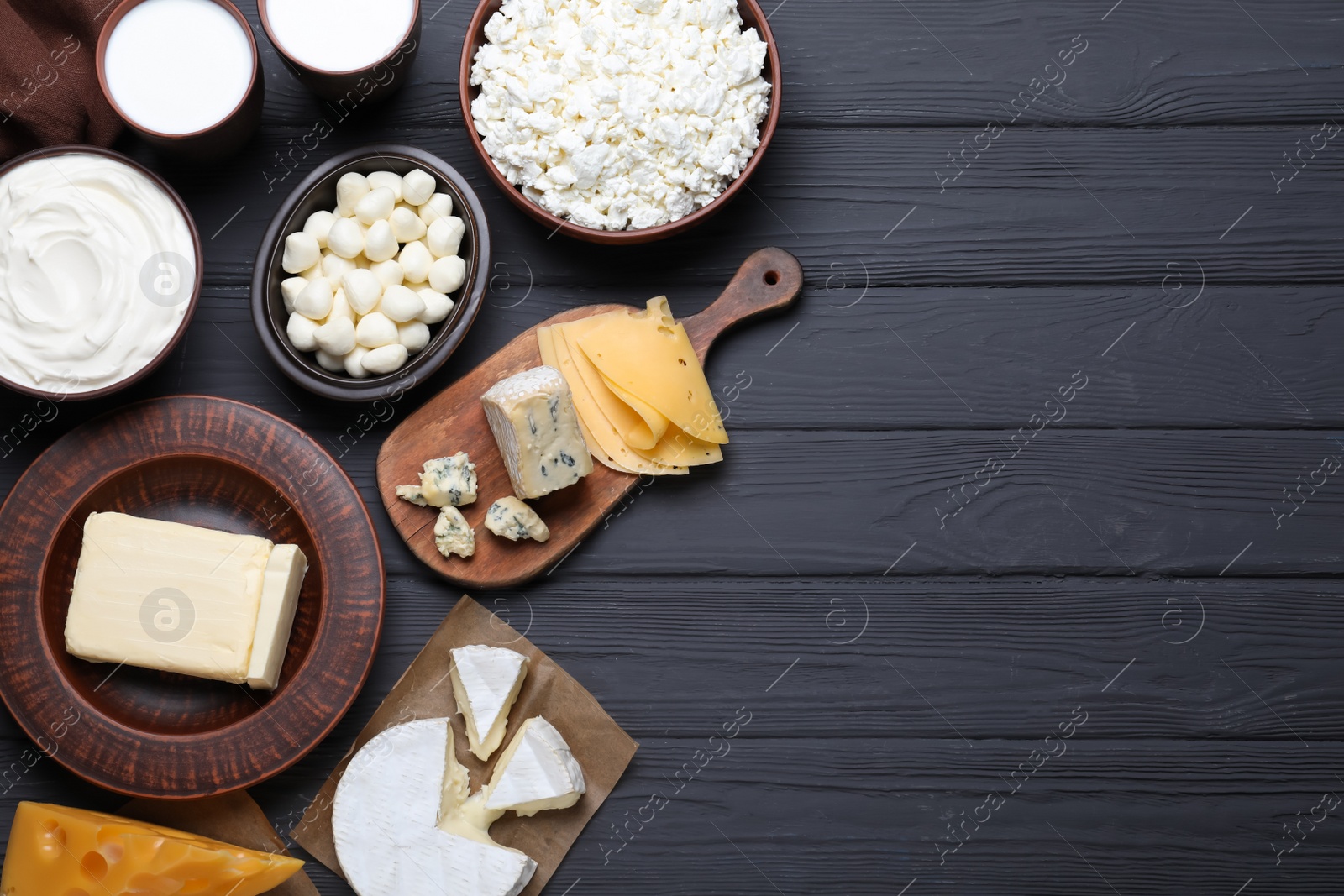 Photo of Clay dishware with fresh dairy products on black wooden table, flat lay. Space for text