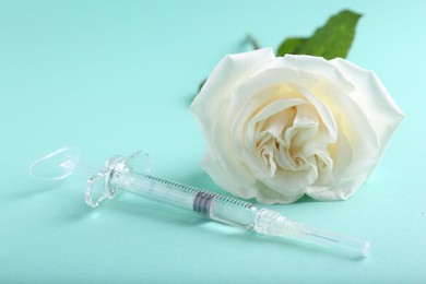 Photo of Cosmetology. Medical syringe and rose flower on turquoise background, closeup