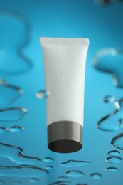 Moisturizing cream in tube on glass with water drops against blue background, low angle view