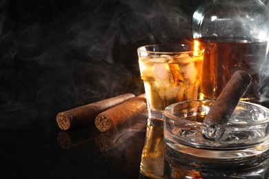 Photo of Smoldering cigar, ashtray and whiskey on black mirror surface