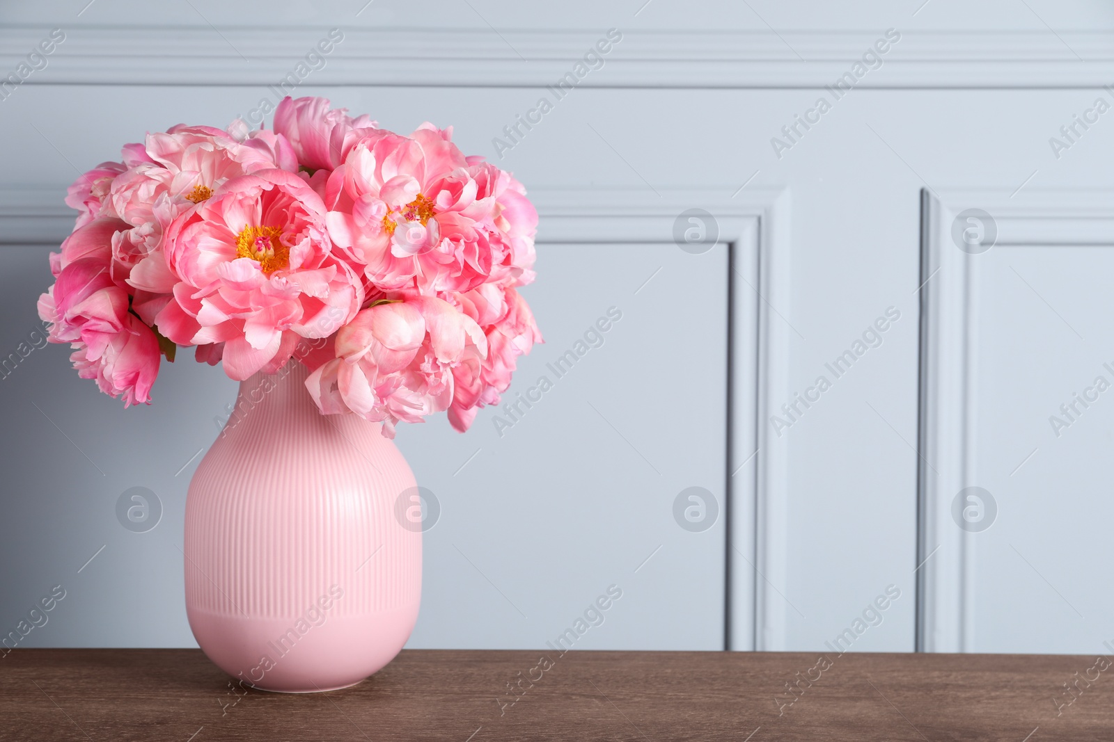 Photo of Beautiful bouquet of pink peonies in vase on wooden table near grey wall. Space for text