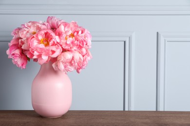 Beautiful bouquet of pink peonies in vase on wooden table near grey wall. Space for text