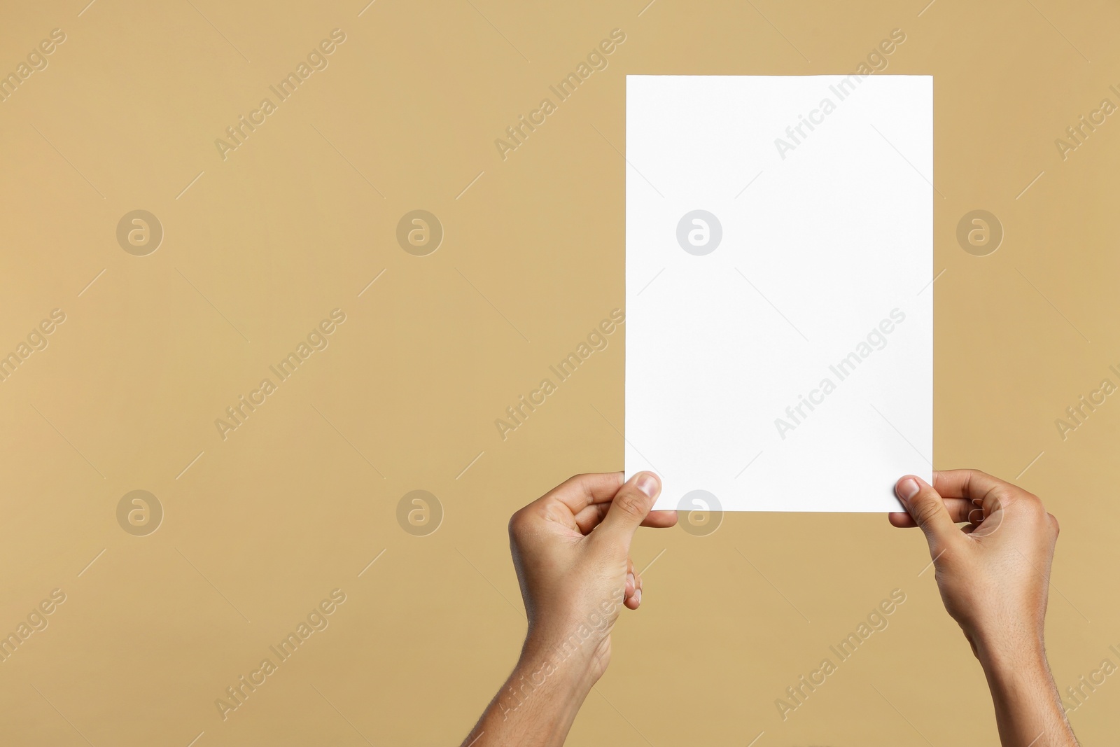 Photo of Man holding sheet of paper on beige background, closeup. Mockup for design