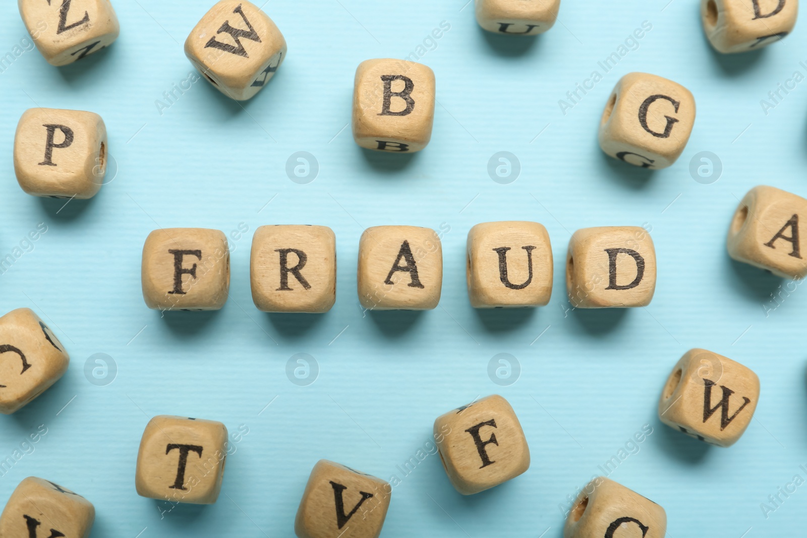 Photo of Word Fraud of wooden cubes with letters on light blue background, flat lay