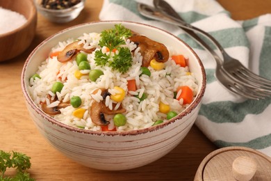 Bowl of delicious rice with vegetables on wooden table, closeup