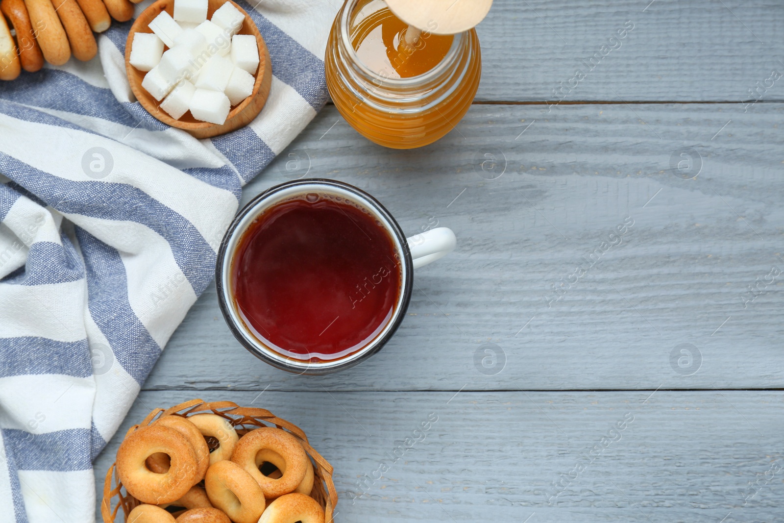 Photo of Flat lay composition with delicious ring shaped Sushki (dry bagels) and mug of tea on light grey wooden table, space for text