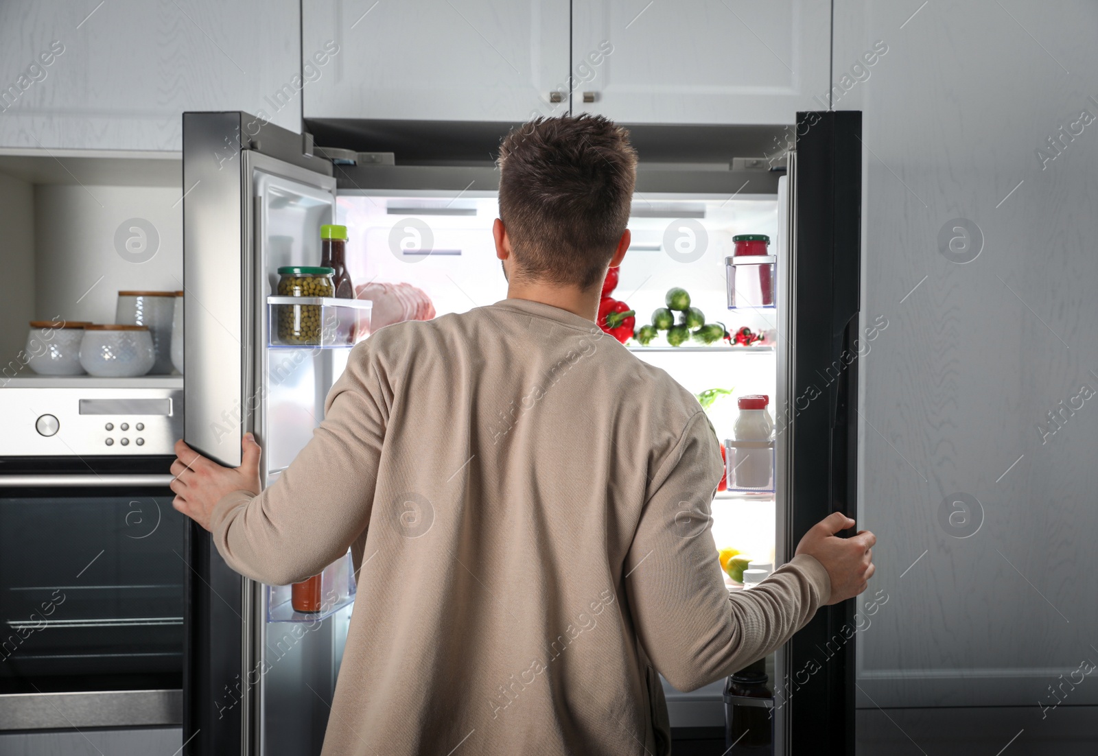 Photo of Young man opening refrigerator indoors, back view