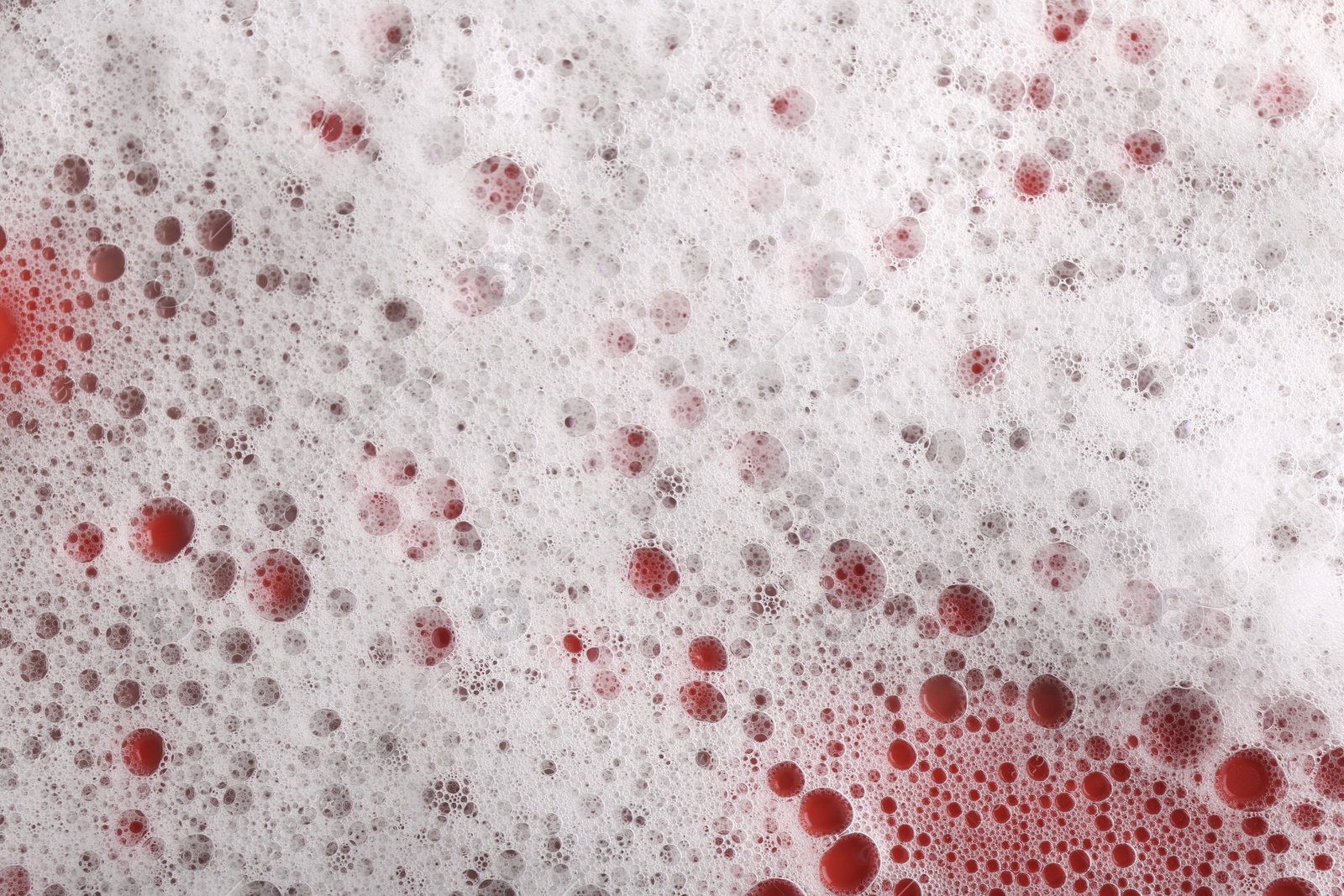 Photo of White foam with bubbles on red background, top view