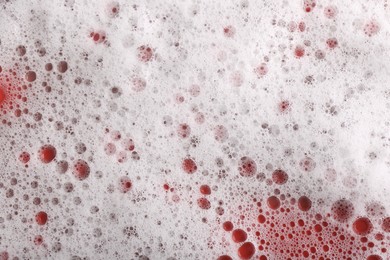 Photo of White foam with bubbles on red background, top view