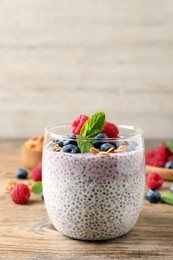 Photo of Delicious chia pudding with berries, granola and mint on wooden table, space for text