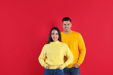 Photo of Happy couple wearing yellow warm sweaters on red background