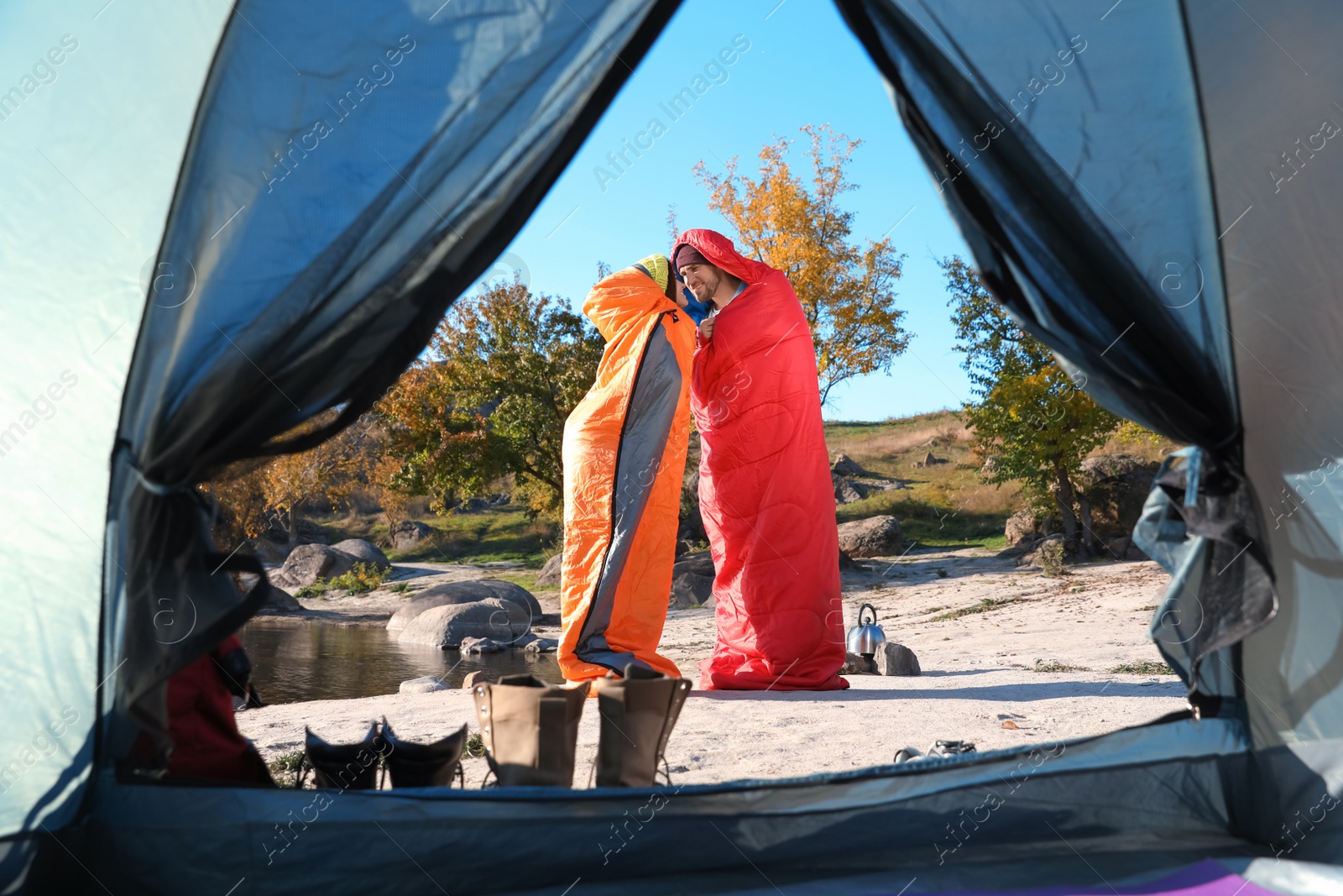 Photo of Cute couple in sleeping bags outdoors, view from camping tent