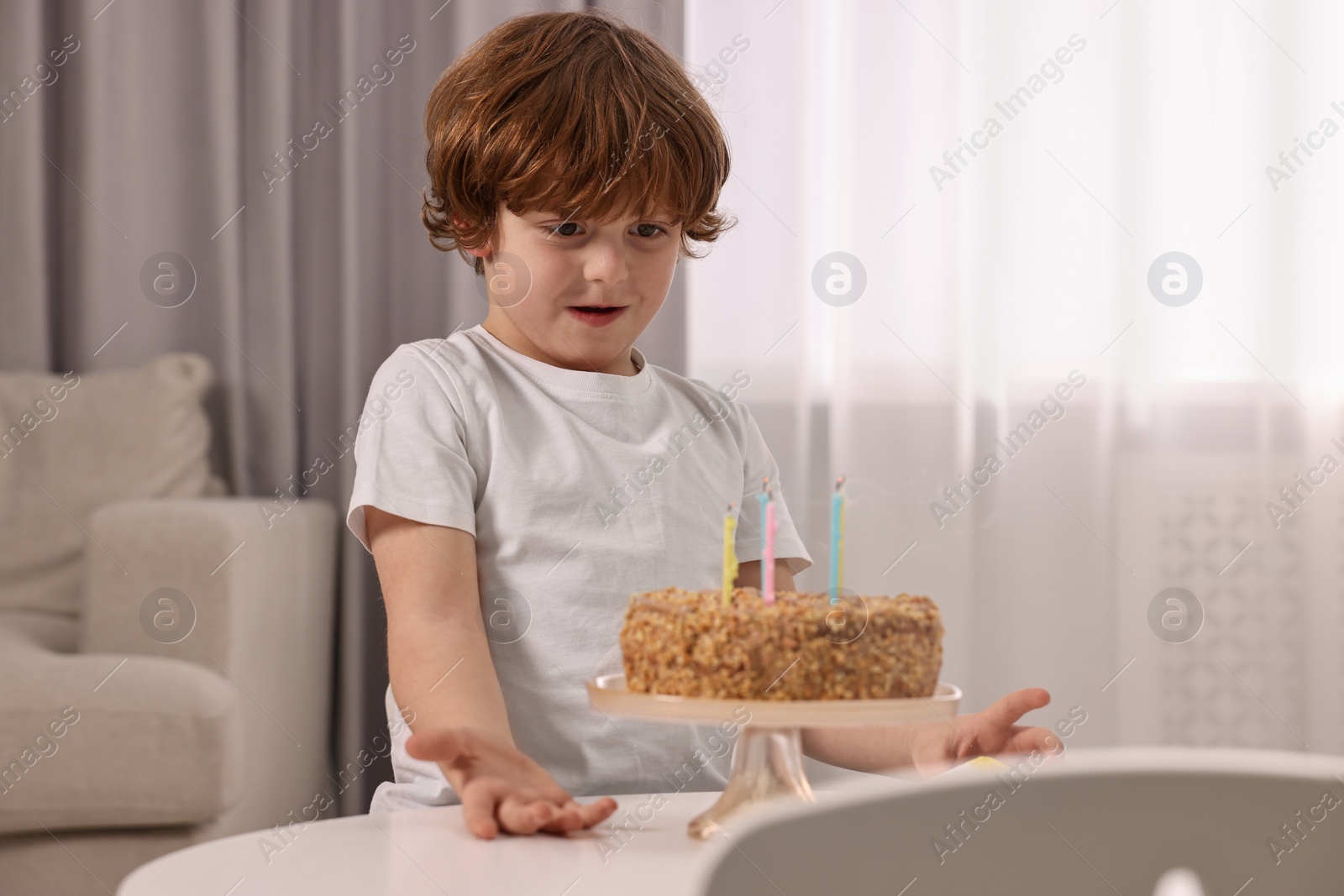 Photo of Cute boy with birthday cake at table indoors