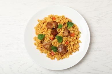 Photo of Plate with delicious rice pilaf on wooden background, top view