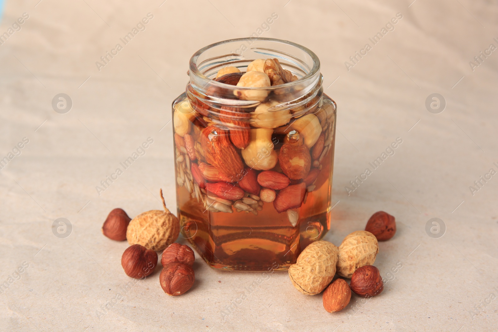 Photo of Jar with different nuts and honey on beige background