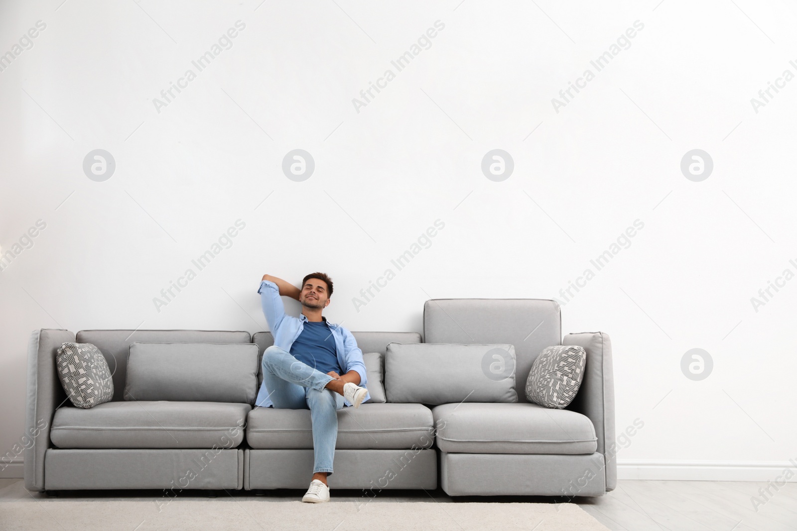 Photo of Young man relaxing on sofa against white wall