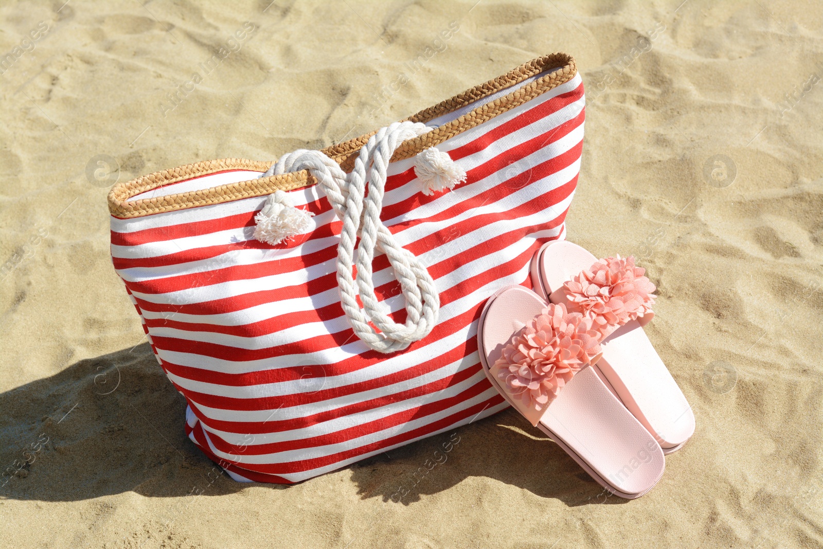 Photo of Stylish striped bag with slippers on sandy beach