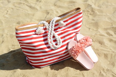 Photo of Stylish striped bag with slippers on sandy beach