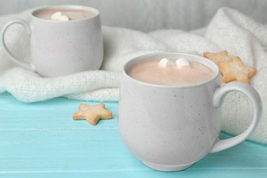 Photo of Composition with delicious cacao drink in cup and blanket on turquoise wooden background