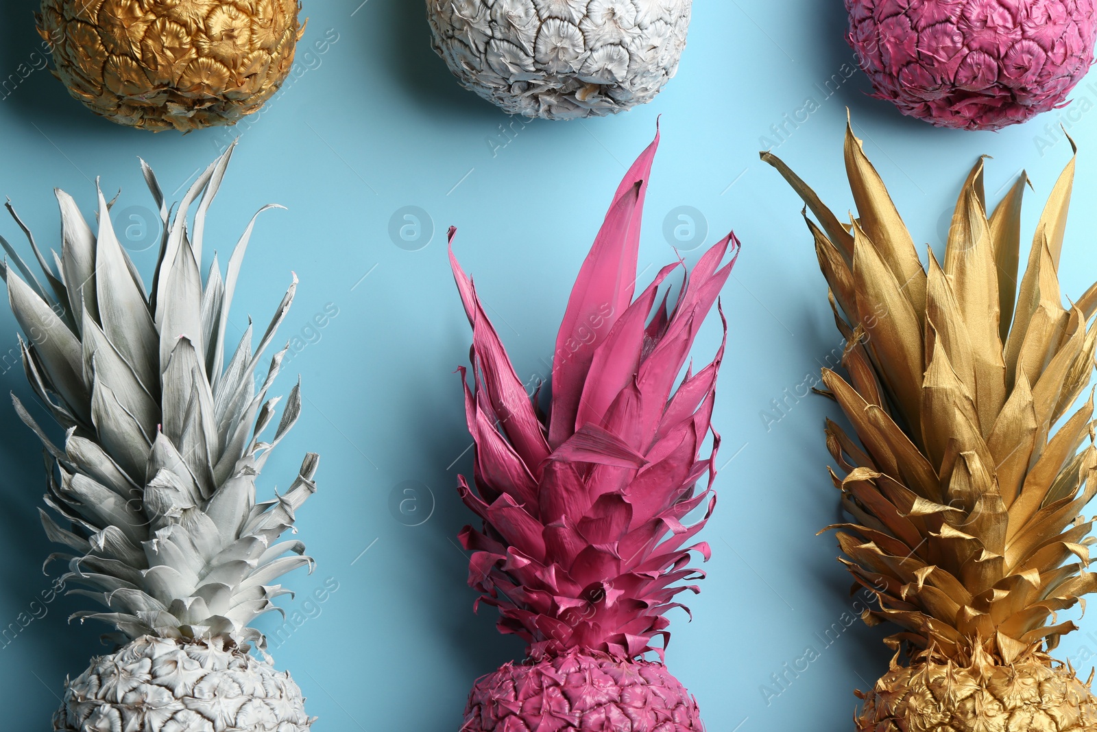 Photo of Different painted pineapples on light blue background, flat lay. Creative concept