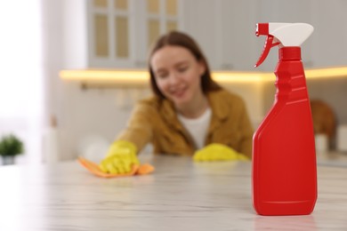 Woman with microfiber cloth cleaning white marble table in kitchen, focus on spray bottle