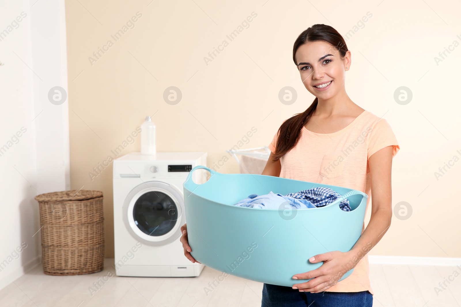 Photo of Young woman with laundry basket near washing machine at home. Space for text