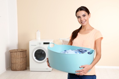 Young woman with laundry basket near washing machine at home. Space for text