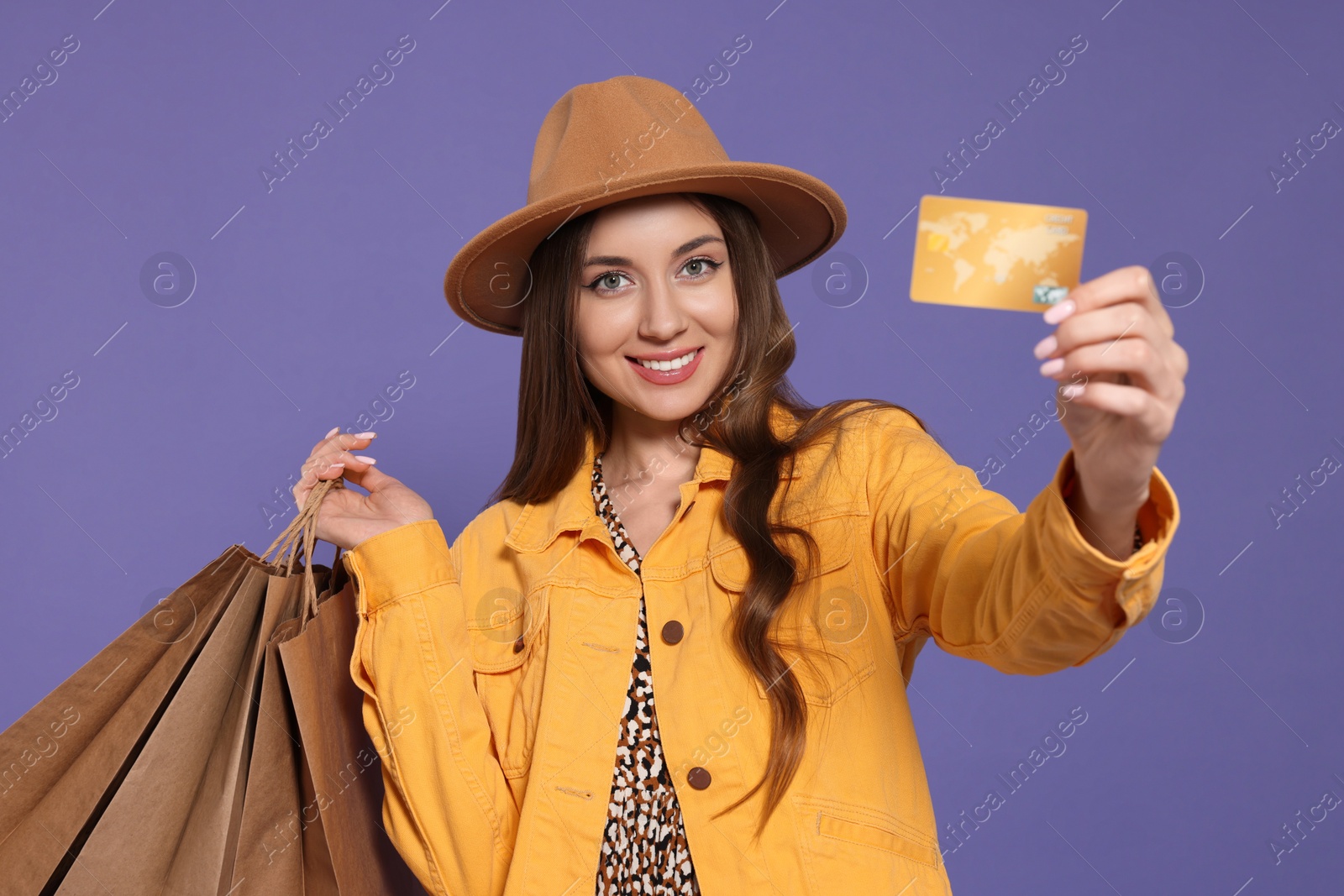 Photo of Stylish young woman with shopping bags and credit card on purple background