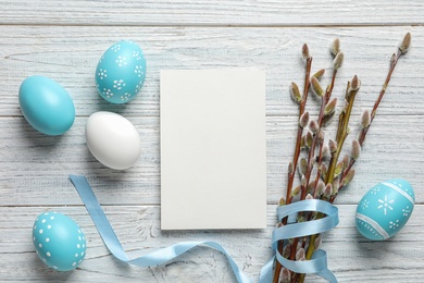 Flat lay composition with painted Easter eggs and blank card on wooden background, space for text