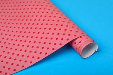Photo of Roll of polka dot wrapping paper on light blue background, closeup