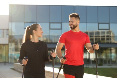 Happy couple practicing Nordic walking with poles outdoors on sunny day