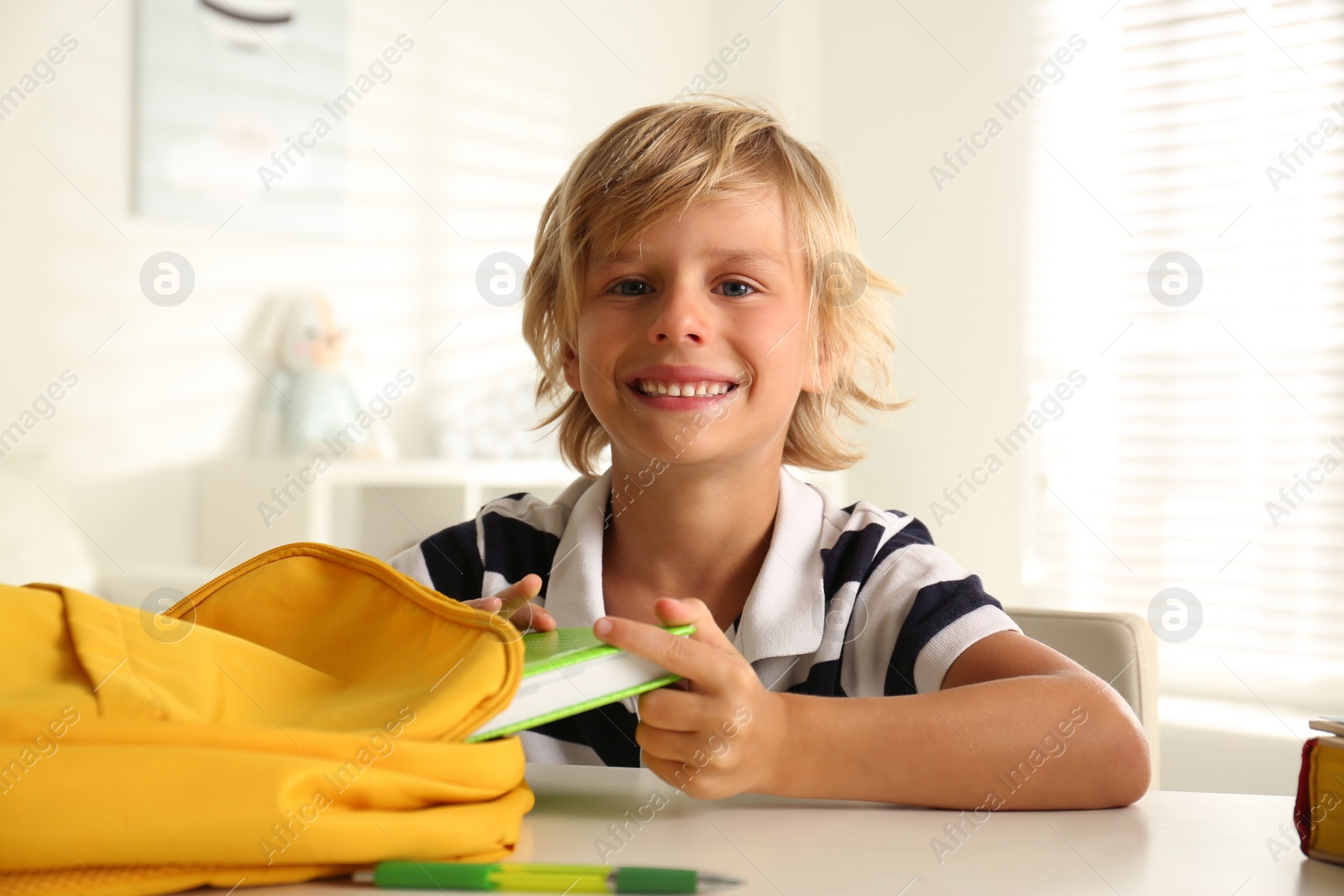 Photo of Little boy taking book from backpack at table indoors. Doing homework