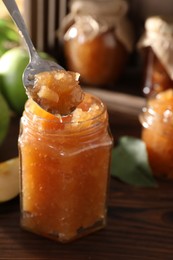 Spoon with delicious apple jam above jar on wooden table, selective focus