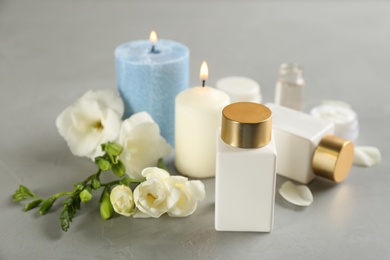 Beautiful spa composition with cosmetic products, flowers and candles on light grey table