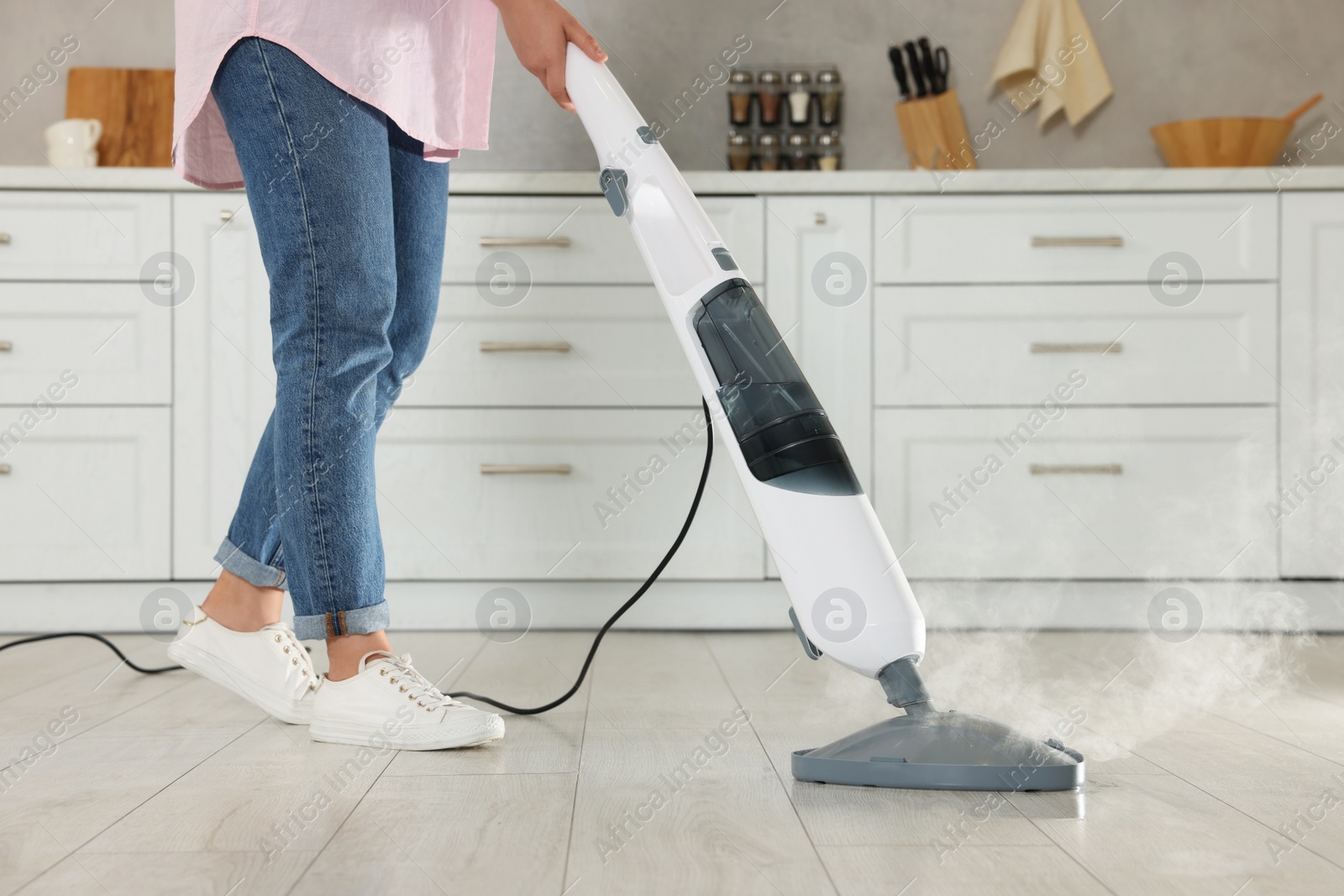 Photo of Woman cleaning floor with steam mop in kitchen at home, closeup