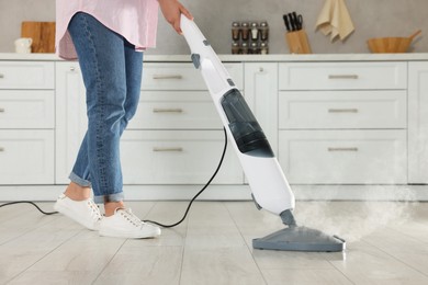 Woman cleaning floor with steam mop in kitchen at home, closeup