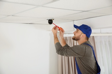 Electrician with screwdriver repairing CCTV camera indoors. Space for text